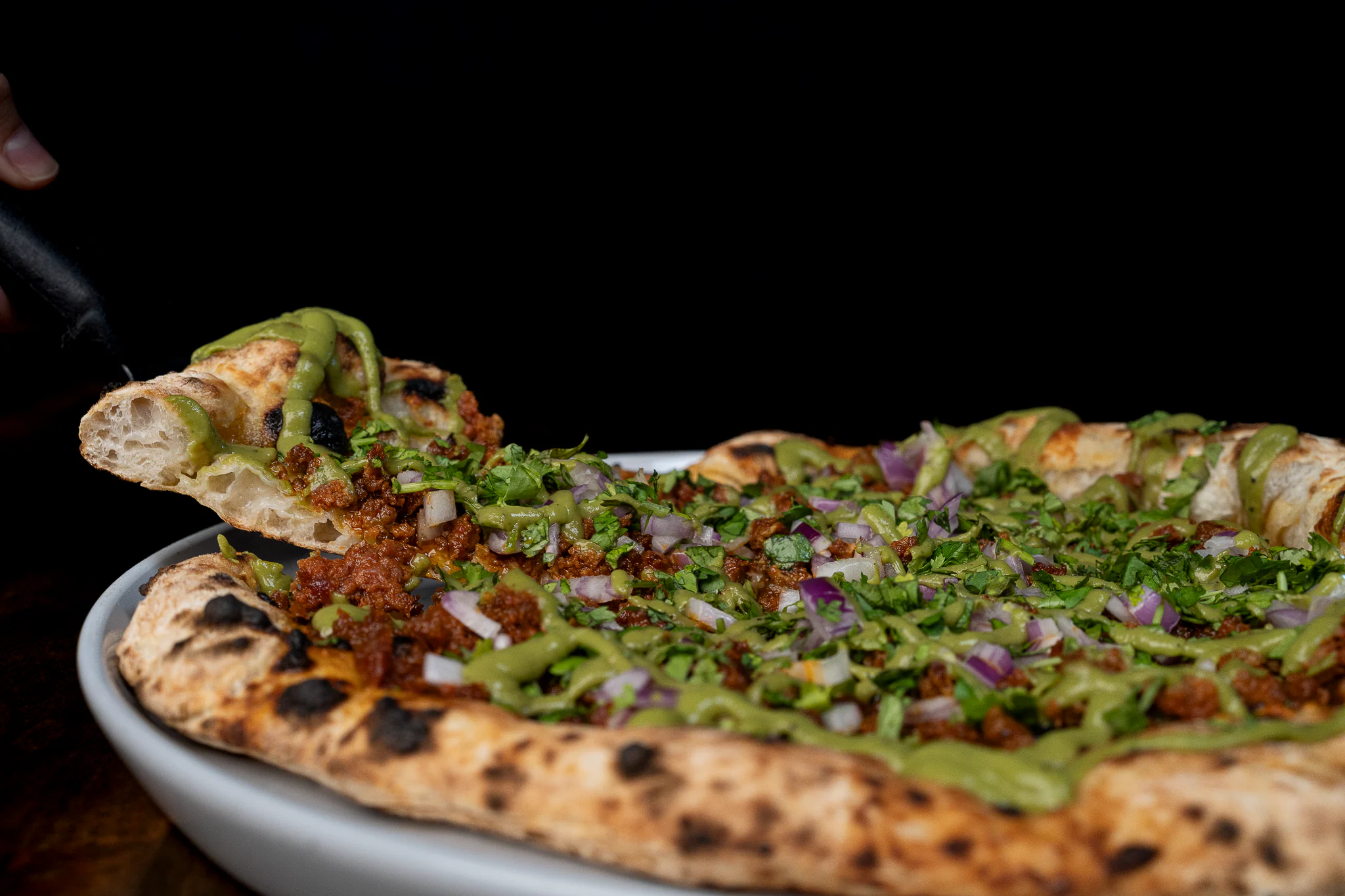 A woman picking up a slice of the Chorizo pizza at El Fornino 