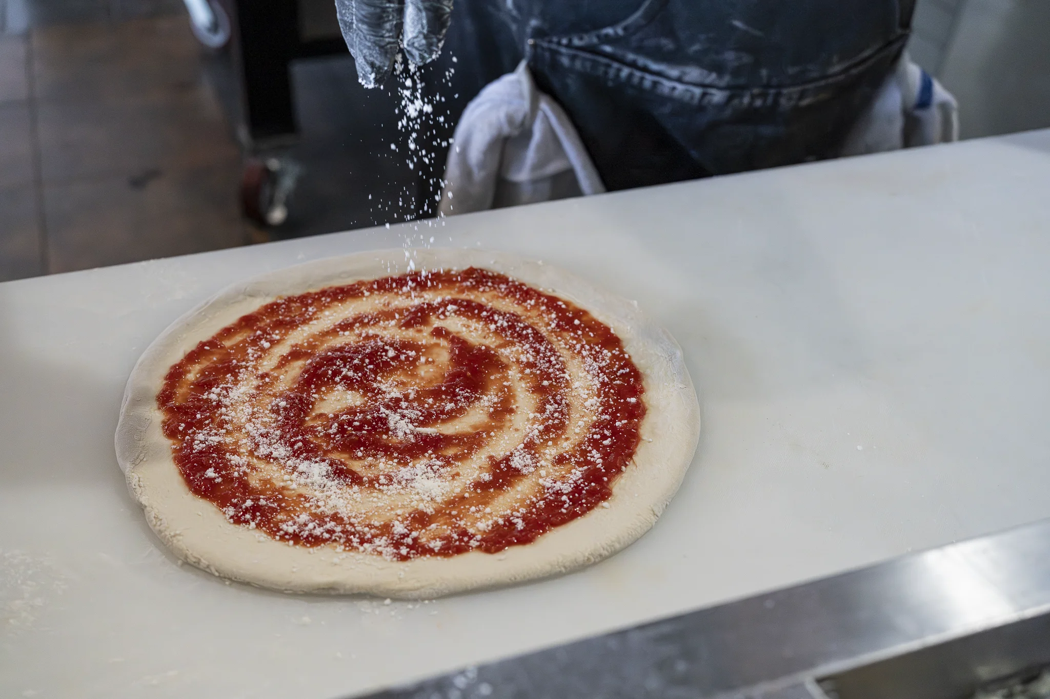 Chef sprinkling cheese onto a pizza with tomato sauce during preparation