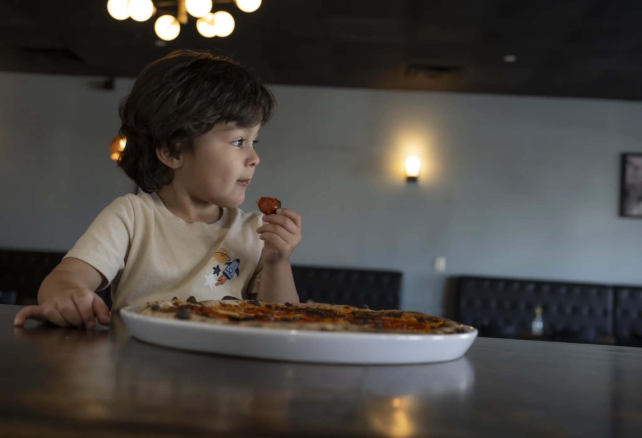 Young child eating a slice of pizza at a table in the El Fornino dining room